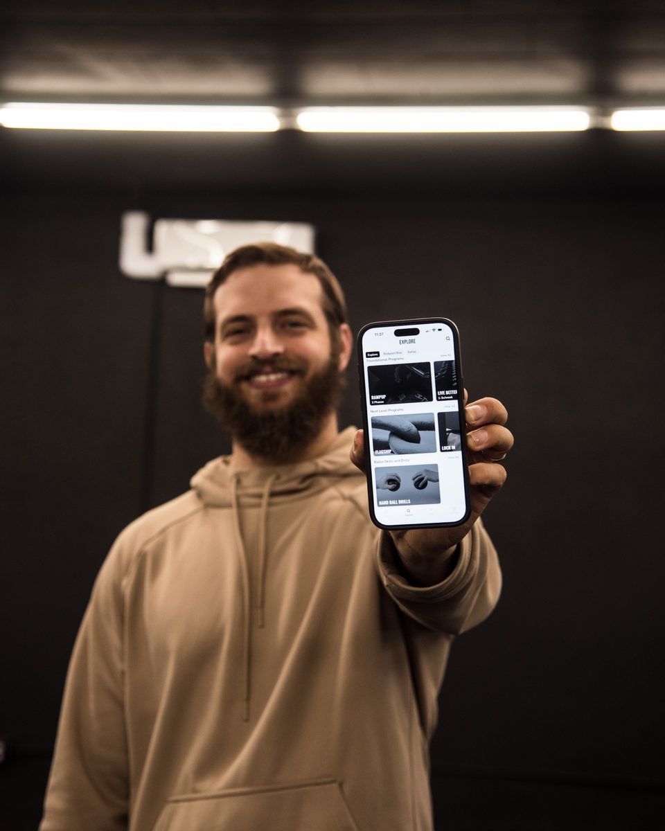 Holding up a phone showing the NW FIT training app's program library