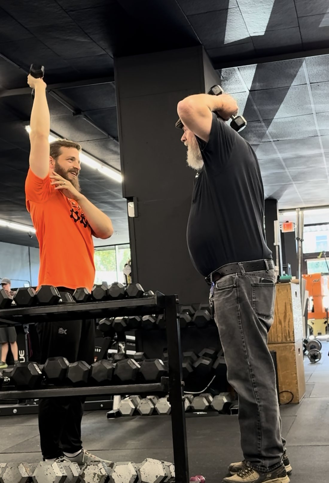 A coach demonstrating an overhead tricep extension next to a member doing the same movement at NW FIT